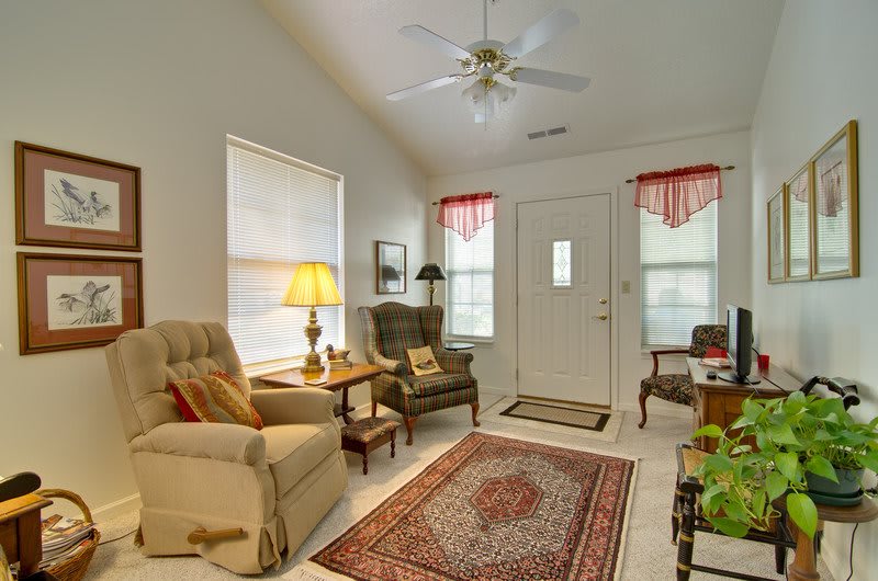 A cozy living room with armchairs, a patterned rug, and a ceiling fan.