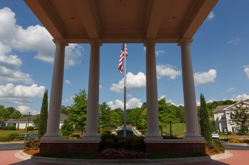 A scenic view of a flagpole framed by large columns with a blue sky and greenery in the background.