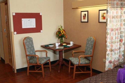 A cozy dining area featuring a small table, two chairs, and a vase of flowers against a warm-toned wall.