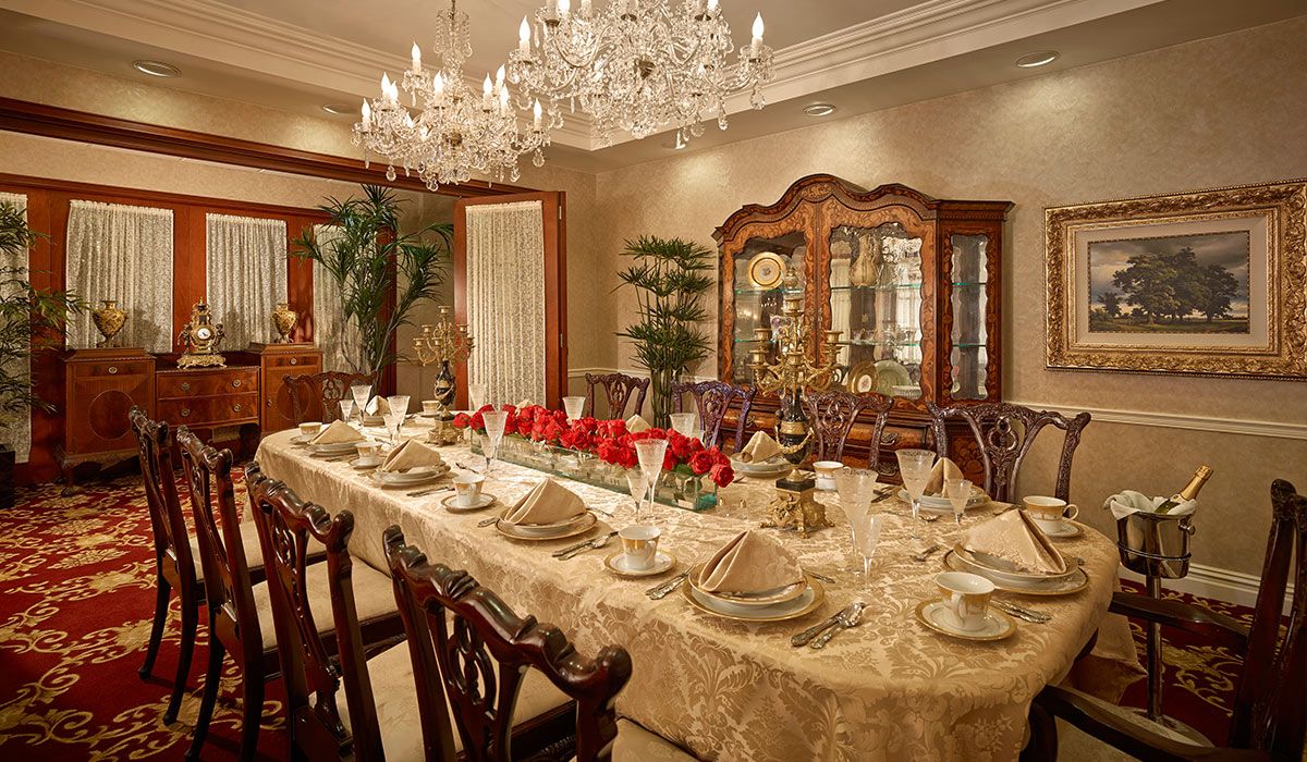 An elegantly set dining room with a luxurious table arrangement, complete with a crystal chandelier and china cabinet.