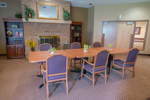 A cozy conference room featuring a long wooden table with purple chairs, complemented by a fireplace and decorative indoor plants.
