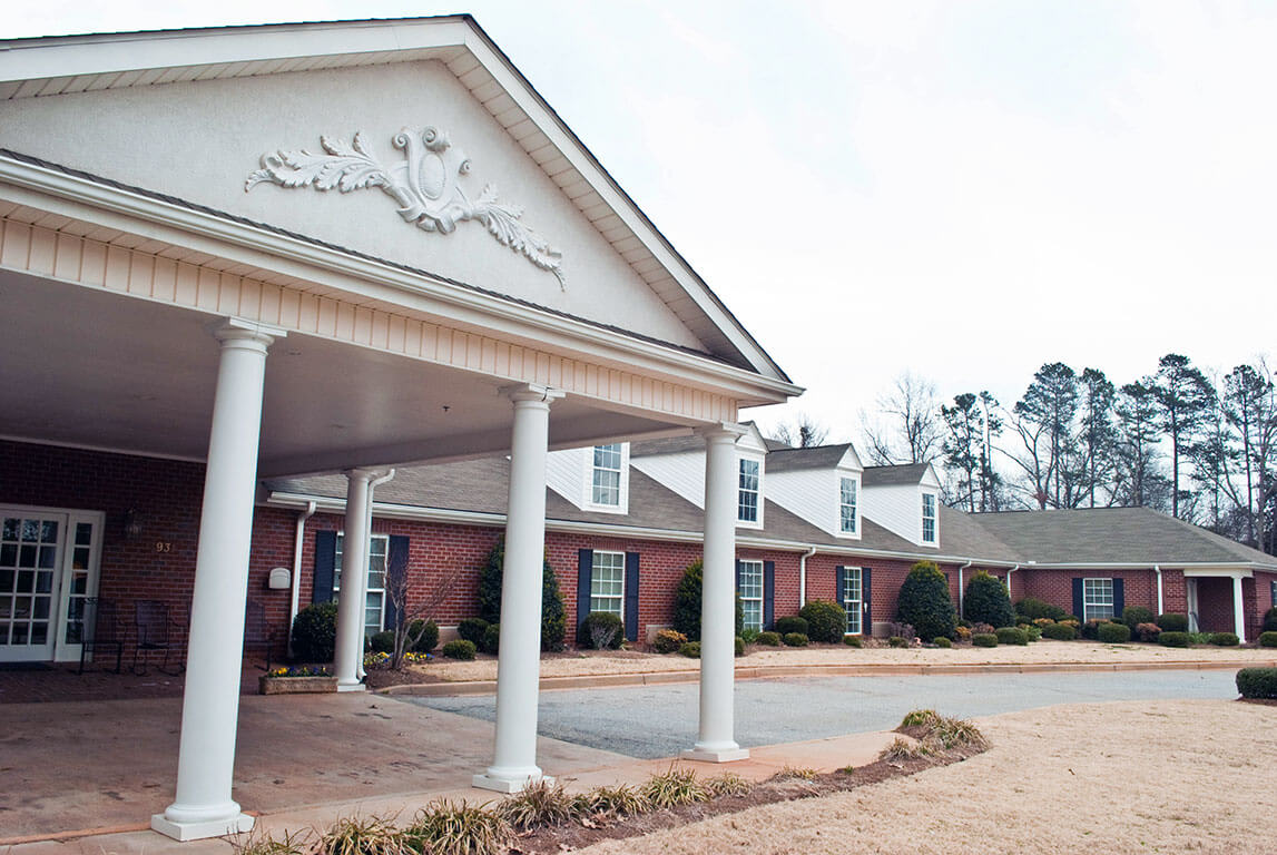Front view of a brick building with white columns and a landscaped entrance.