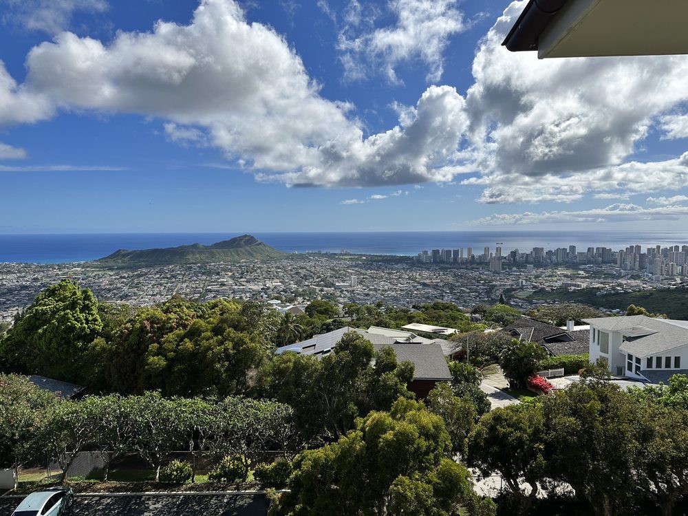 A scenic view overlooking a city with the ocean in the background and clouds scattered across a blue sky.