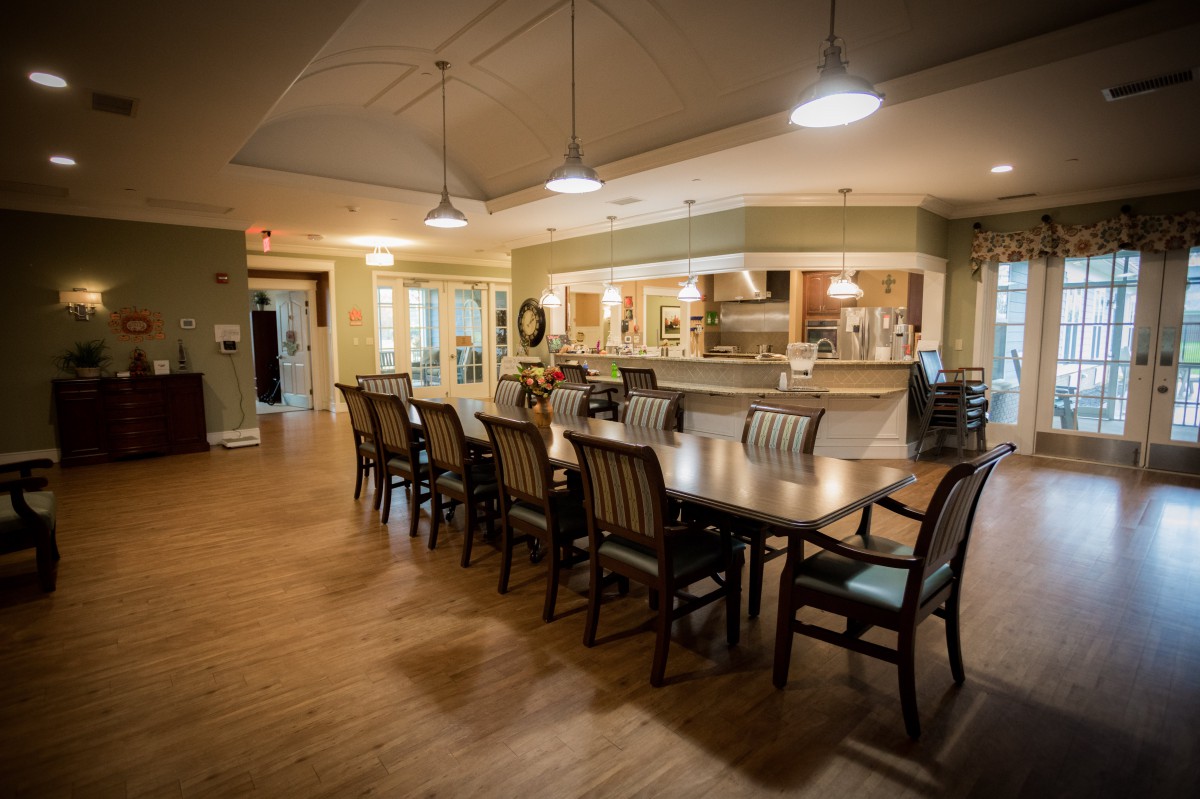 A spacious dining room with a long wooden table and chairs, adjacent to a kitchen area.