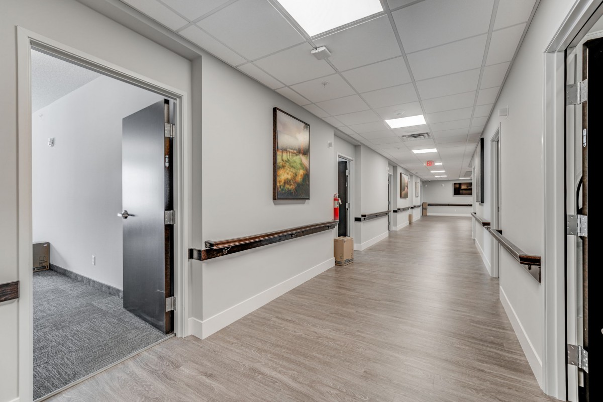 A clean and modern hospital corridor with open doors and a handrail along the wall.