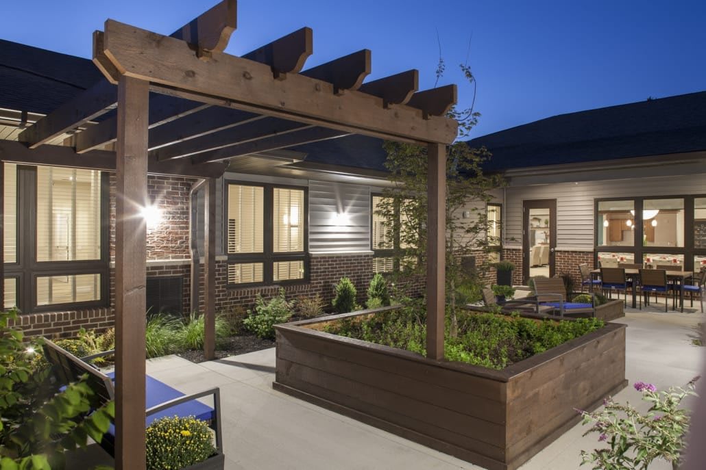 A modern outdoor patio with a wooden pergola and garden at dusk.