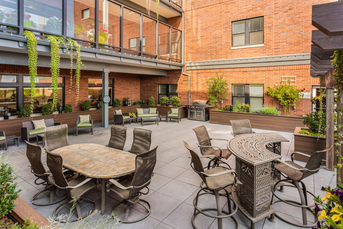 A cozy courtyard with tables and chairs surrounded by brick walls and greenery.