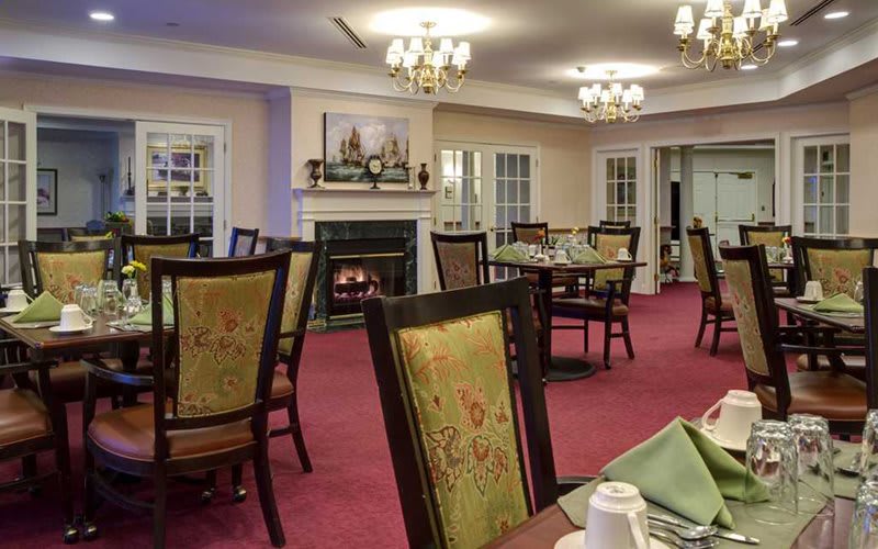 A cozy dining room with elegant chandeliers, a warm fireplace, and neatly arranged tables and chairs.