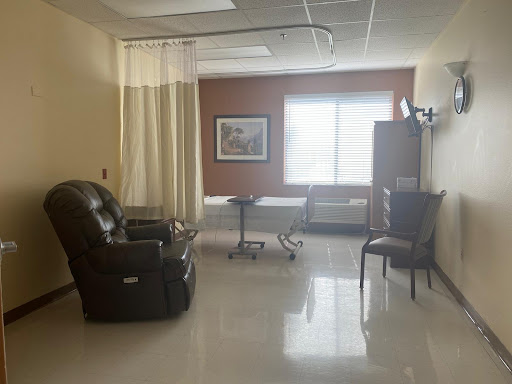 A well-lit hospital room featuring a comfy chair, a small table, and natural light coming through the window.