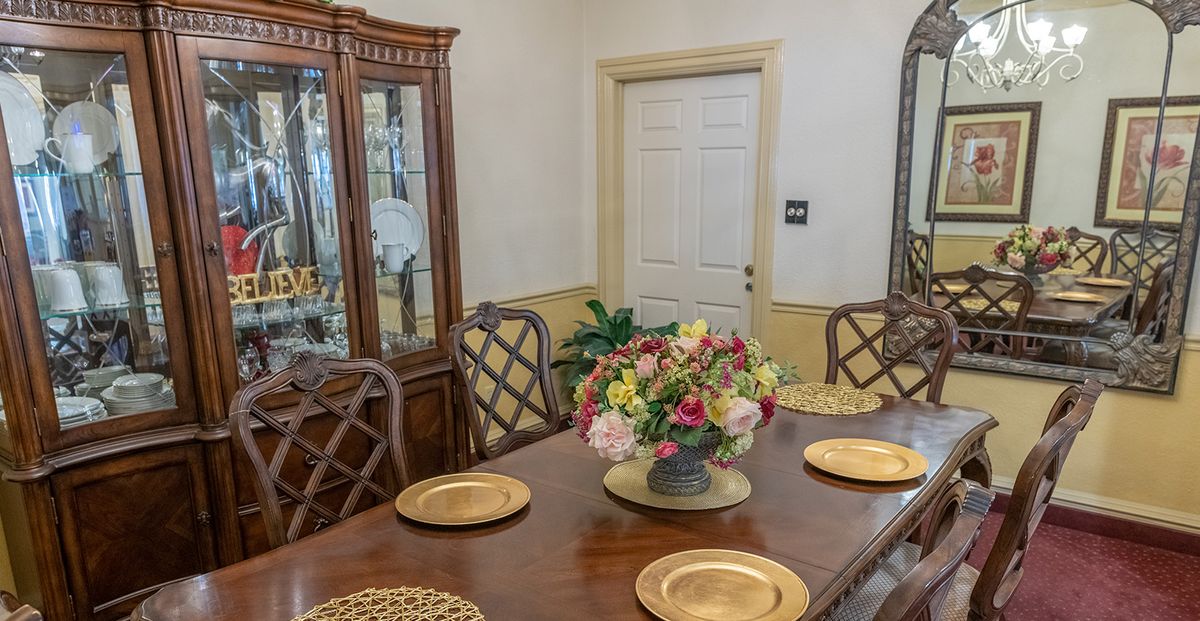 A dining room with a wooden table set for a meal, featuring a central flower arrangement and surrounded by elegant chairs.