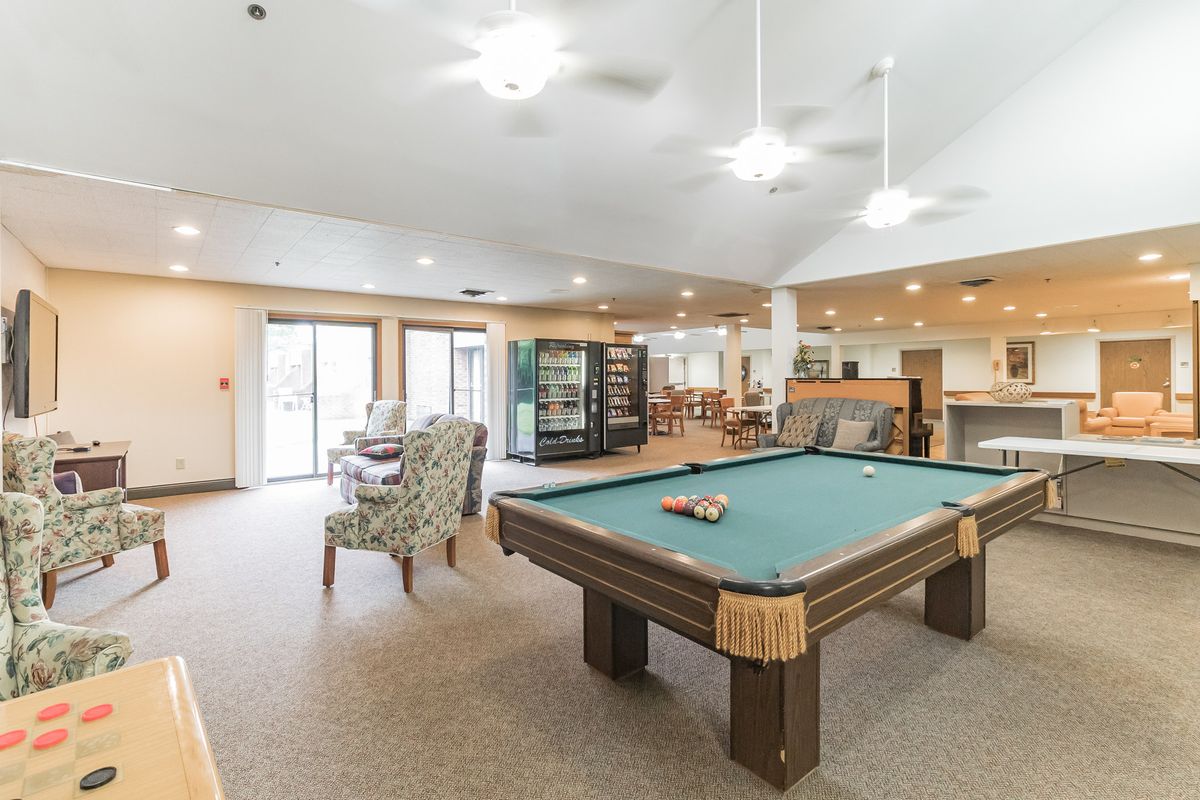 A spacious game room featuring a pool table with comfortable seating and bright lighting.