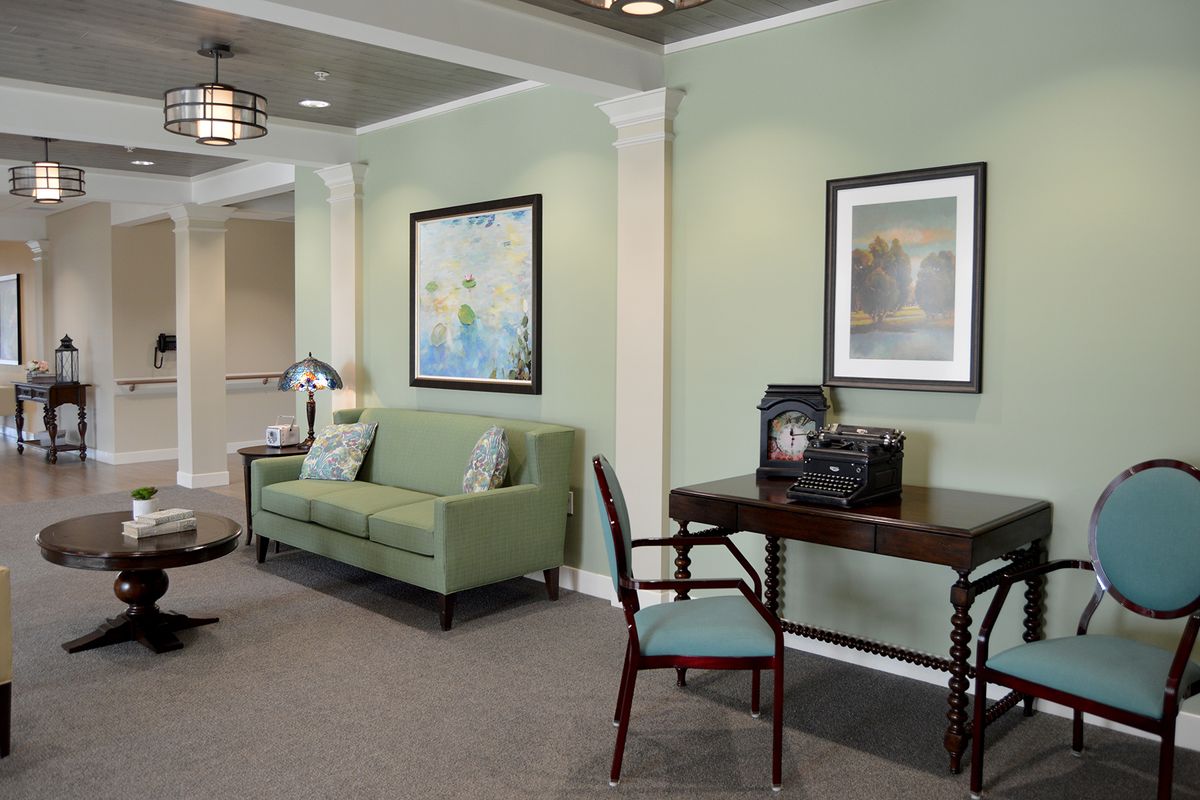 A cozy living room with a green sofa, desk, and artwork on the walls.