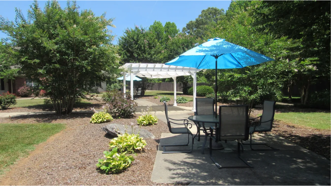 A tranquil garden patio with a table, chairs, and a blue umbrella.
