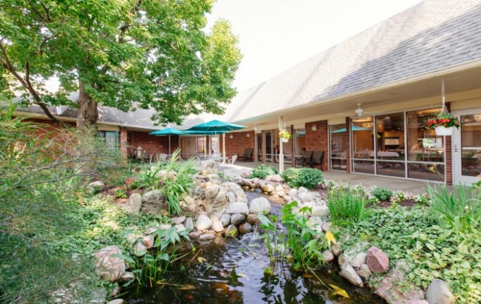 A serene outdoor garden with a pond and surrounding landscaping, adjacent to a building with patio umbrellas.