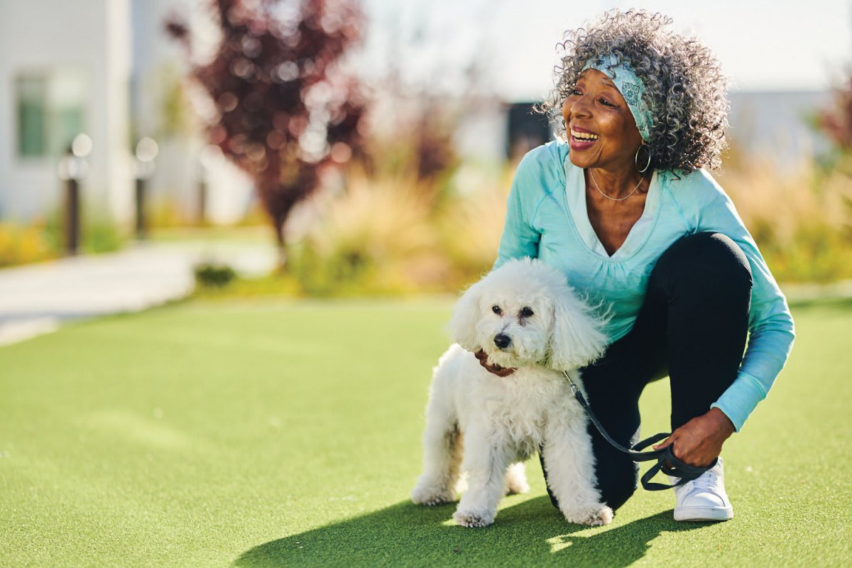 A woman enjoys a sunny day in the park with her poodle.