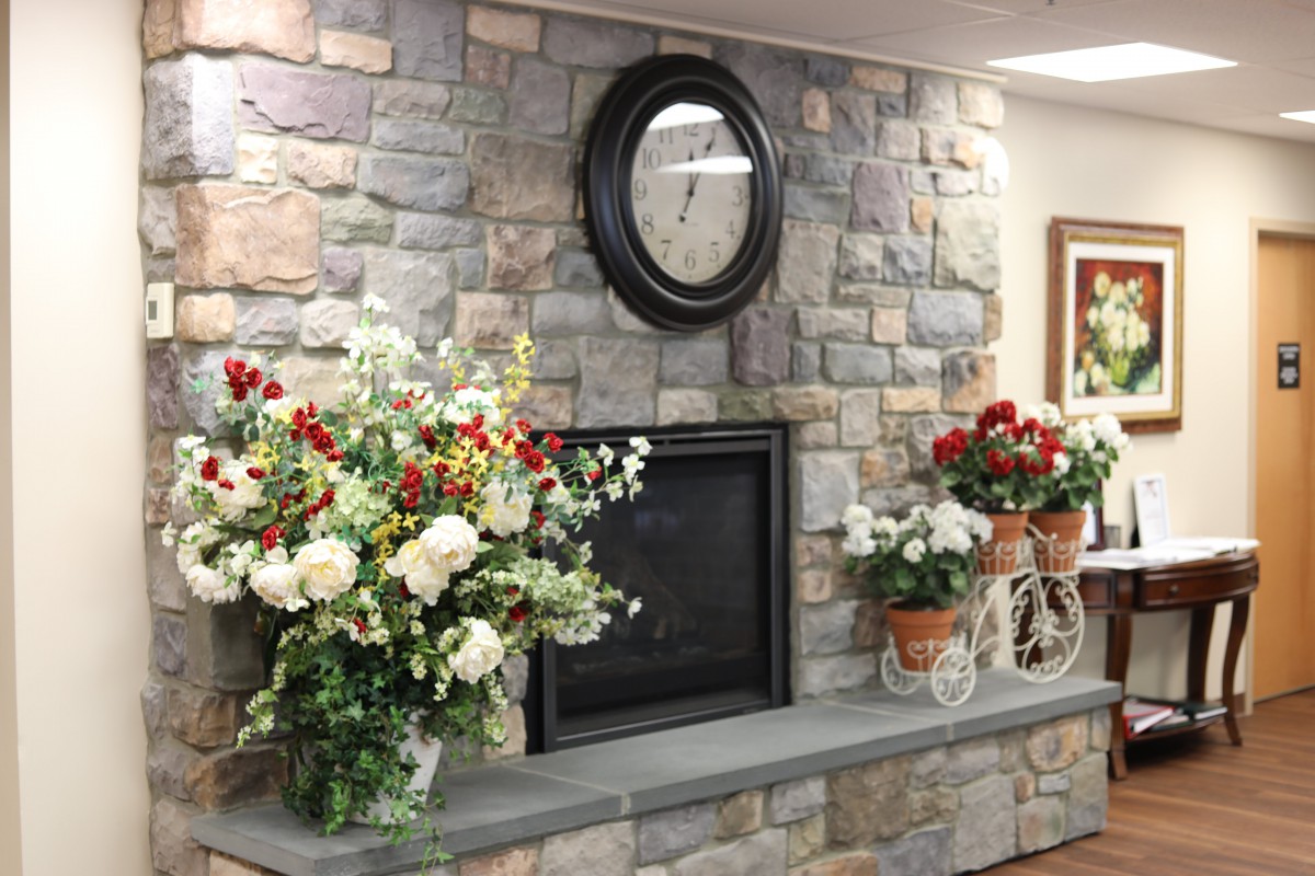 A cozy room with a stone wall fireplace adorned with vibrant floral arrangements and a clock above.