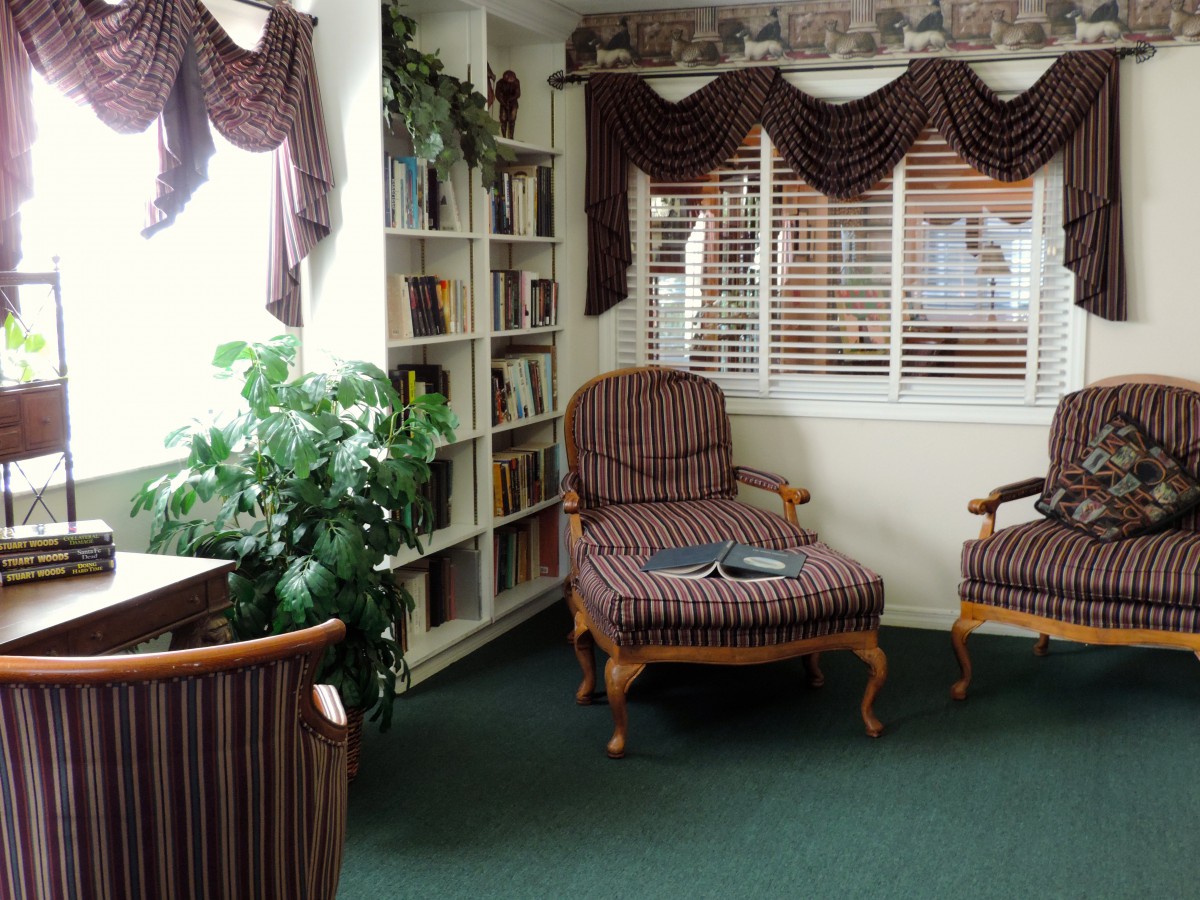 A cozy living room area with armchairs, a bookshelf, and decorative curtains.