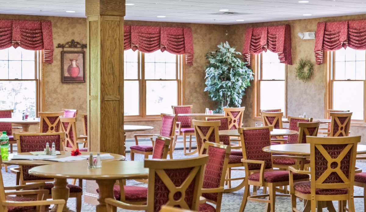 An inviting dining area with red cushioned chairs, wooden tables, and natural light from large windows.