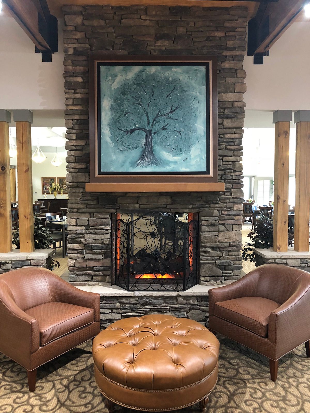 A cozy seating area with a stone fireplace and leather armchairs, adorned by a tree painting above the mantel.