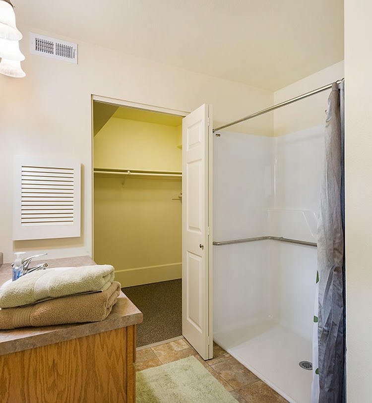 A bathroom with a shower and an adjacent closet, featuring folded towels on the counter.