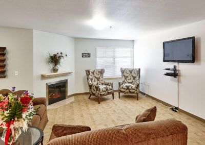 A cozy living room with a fireplace, armchairs, and a wall-mounted TV.