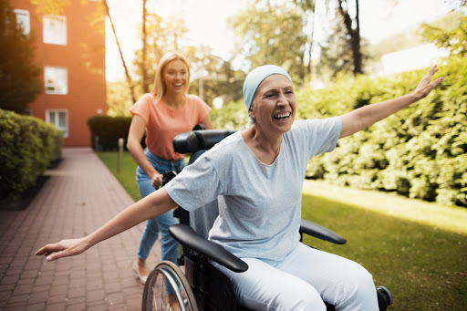A caregiver joyfully pushes a woman in a wheelchair through a beautiful outdoor setting, showcasing companionship and support.