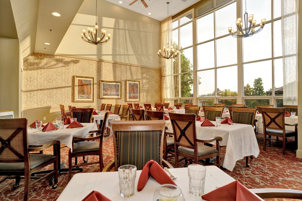A beautifully lit restaurant dining room with elegant table settings and large windows.
