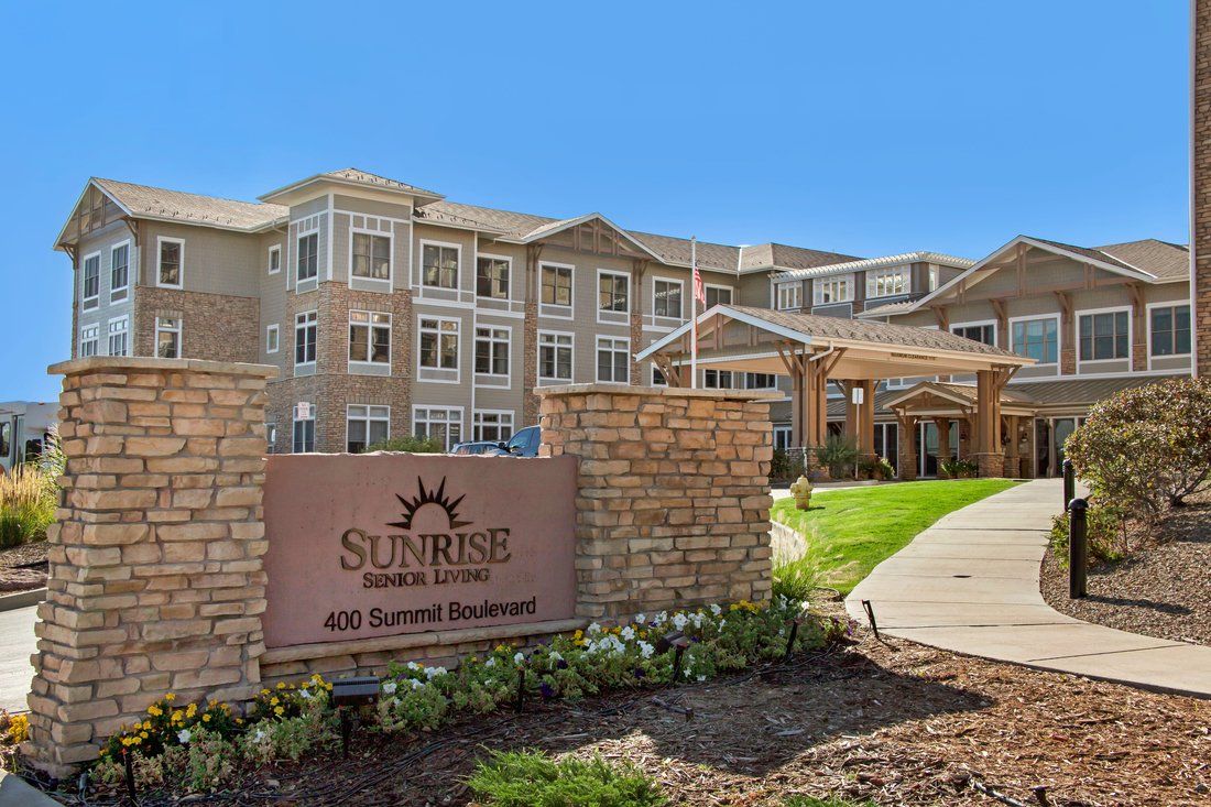 A modern senior living facility with a well-maintained garden and clear blue sky.