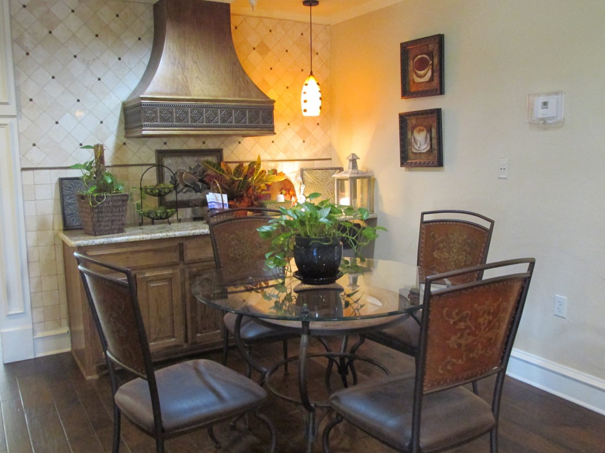A cozy kitchen dining area with a glass-top table surrounded by four chairs, decorated with plants and warm lighting.