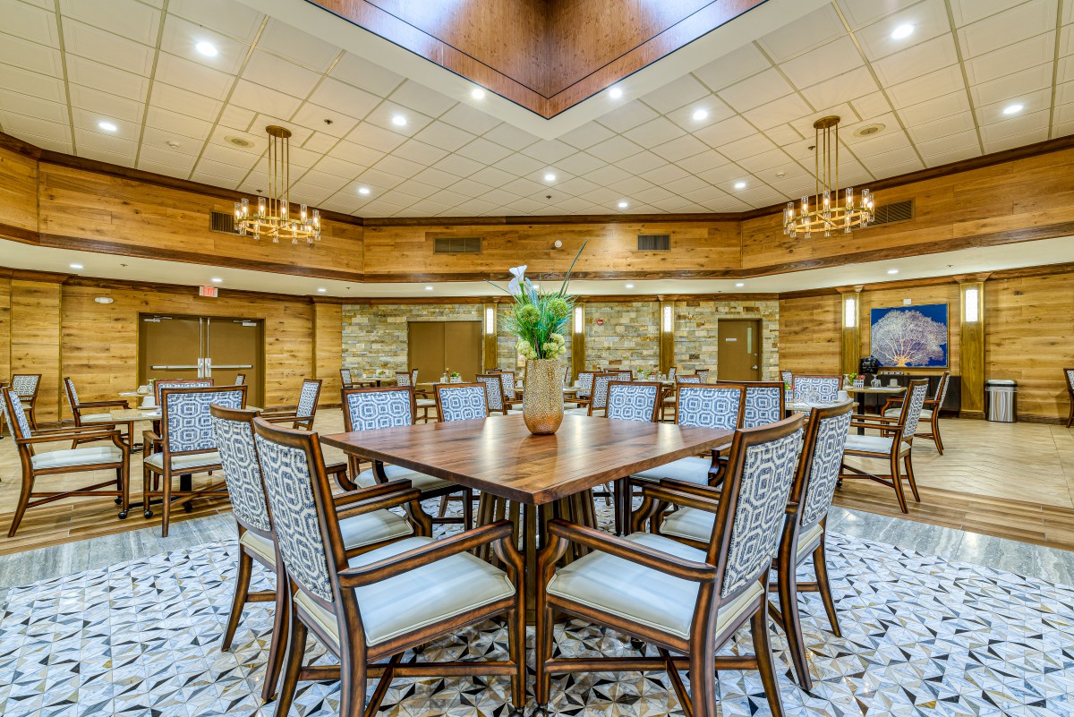 A spacious, modern conference room with a large table surrounded by chairs, featuring wooden accents and elegant ceiling lighting.