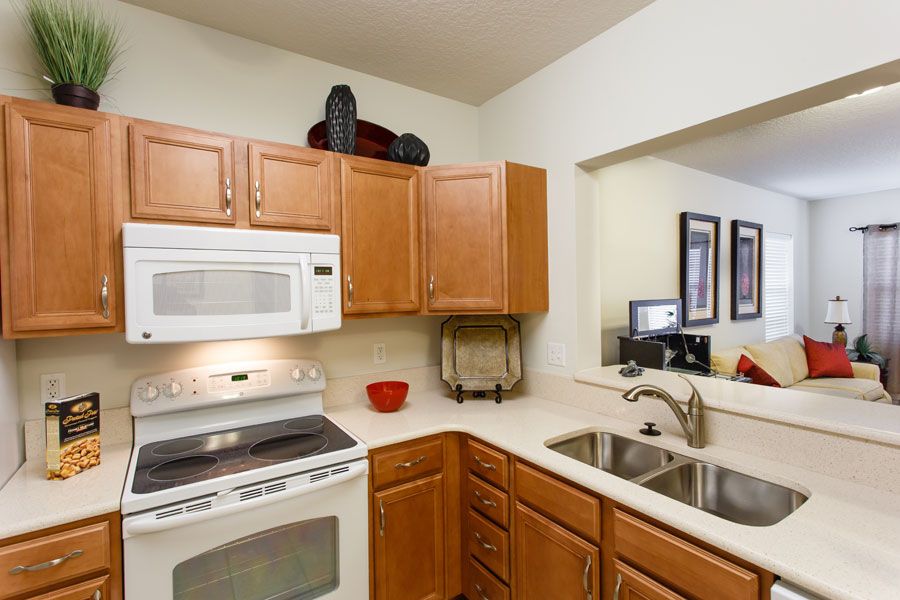 A modern kitchen with wooden cabinets, a microwave, stove, and double sink.