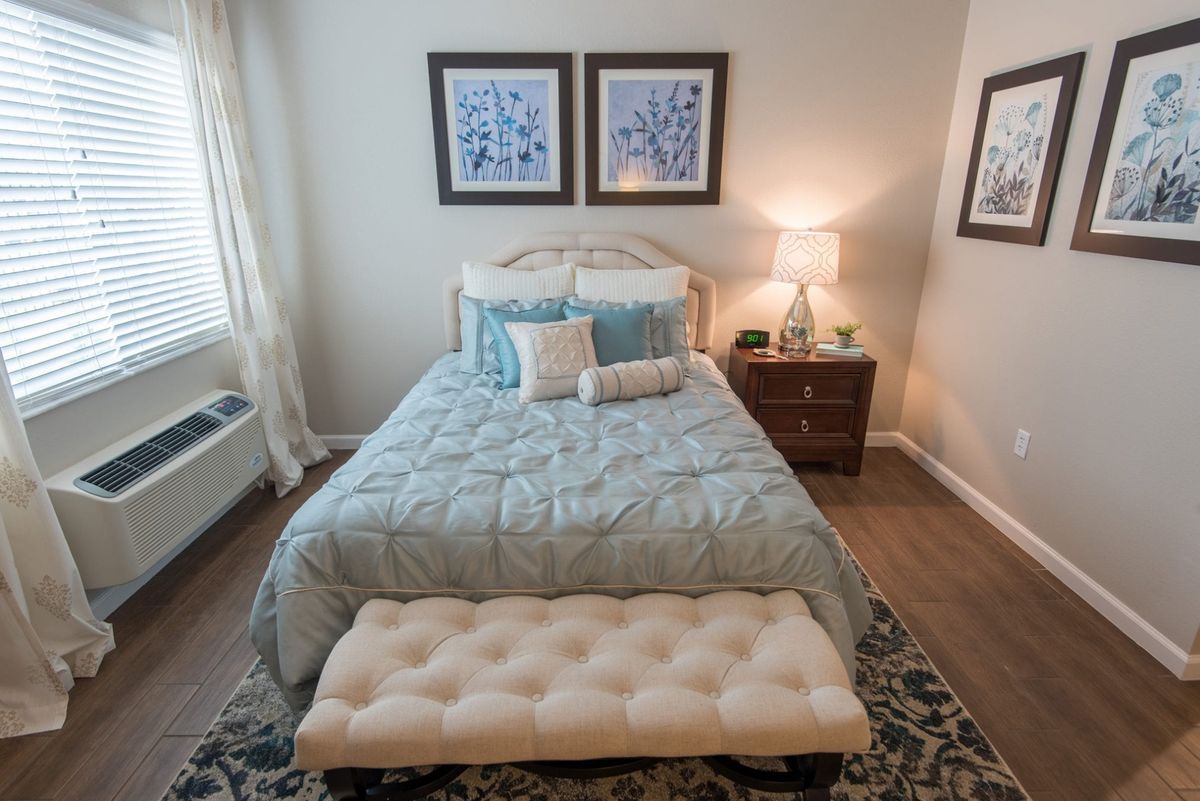 A cozy bedroom with a neatly made bed, nightstand, and soft lighting.