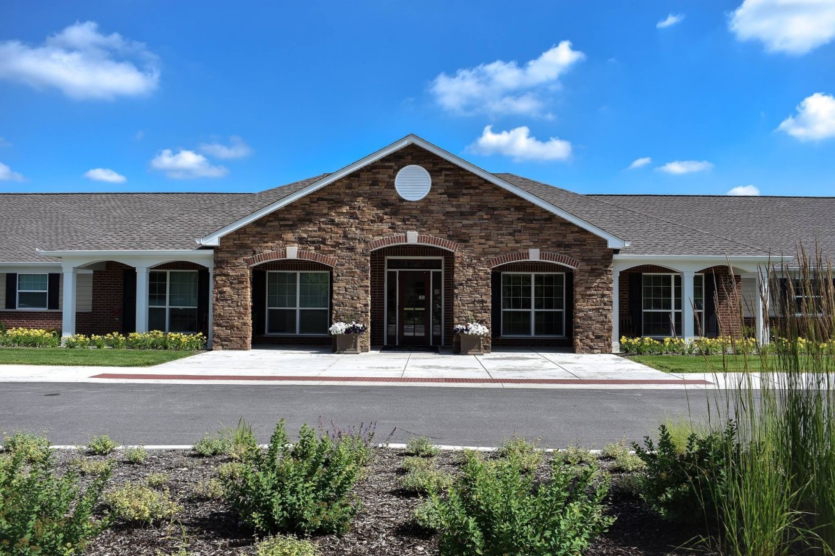 A modern brick building under a bright blue sky with white clouds, surrounded by a driveway and landscaping.