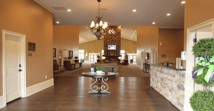 A spacious and modern lobby featuring a central table, chandelier, stone fireplace, and wood flooring.