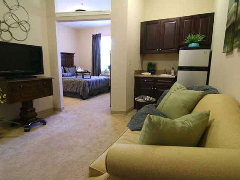 A cozy apartment interior featuring a living area with a sofa and TV, leading into a bedroom and kitchenette.