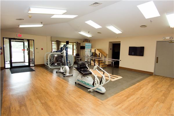 A well-lit gym with various exercise equipment and wooden flooring.