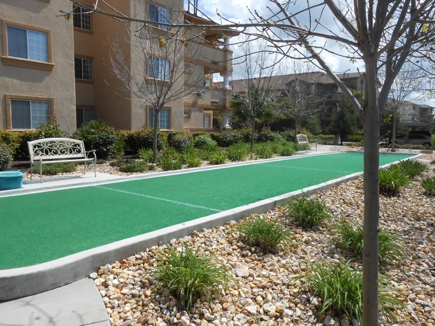 A landscaped outdoor area with a green court and benches beside an apartment building.