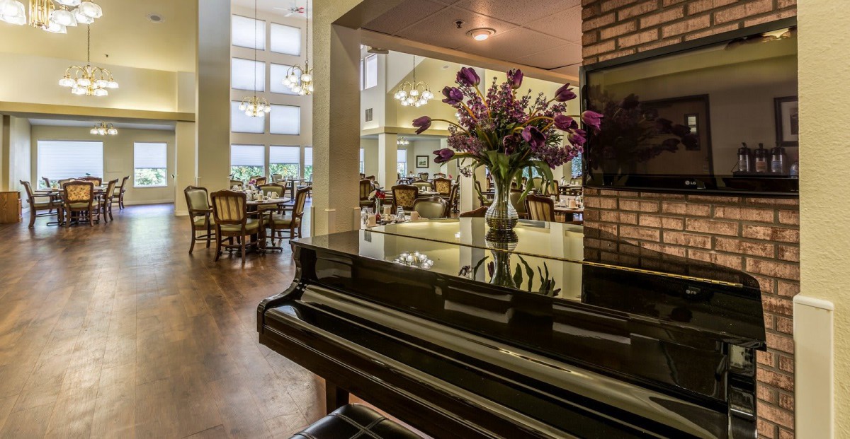 A stylish interior with a grand piano and a dining area, featuring elegant floral decor.