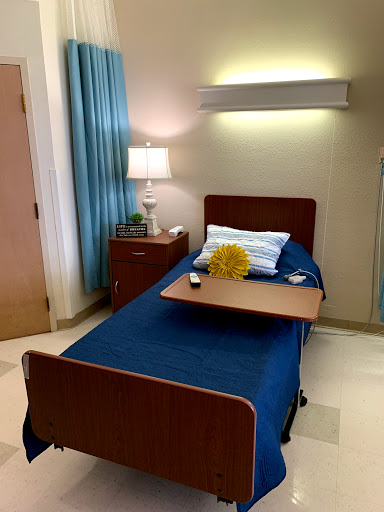 A well-lit patient room featuring a hospital bed, bedside lamp, and decorative touches.