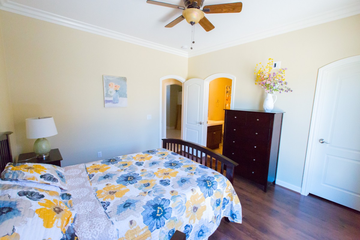 A well-lit bedroom with a floral bedspread, wooden furniture, and ceiling fan.