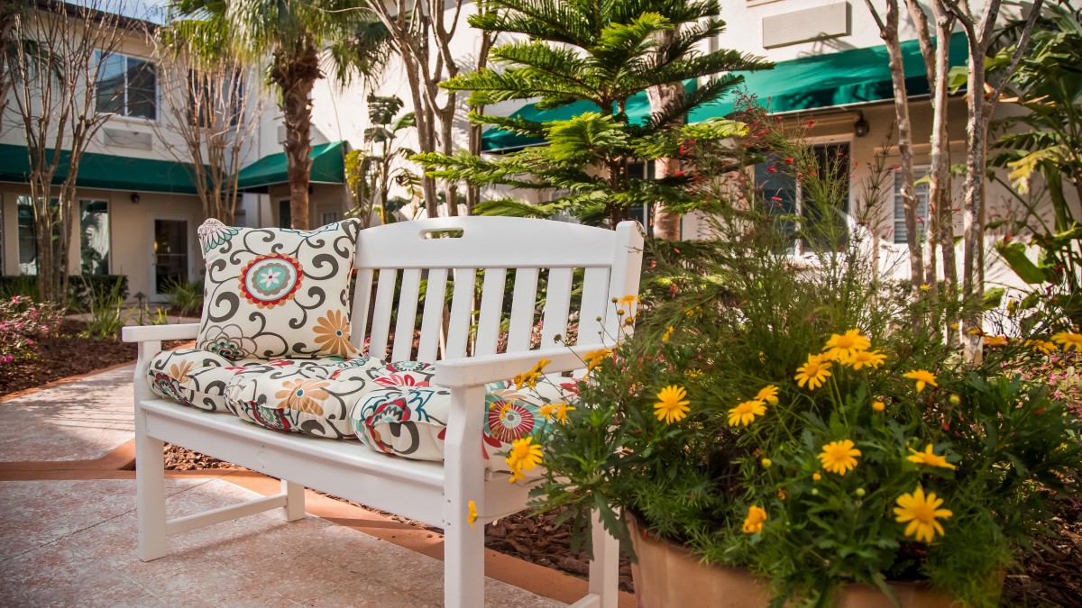 A charming outdoor bench with colorful cushions surrounded by vibrant plants and flowers.