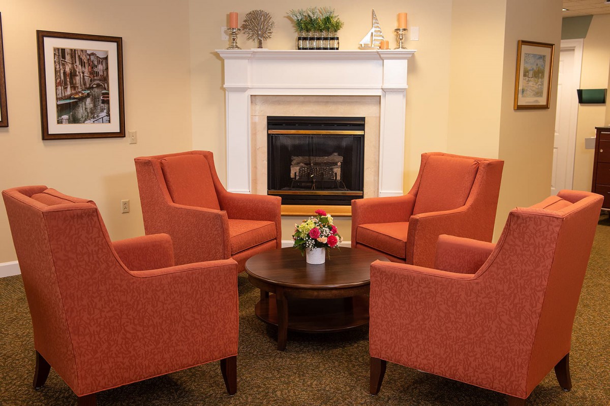 A cozy living room setup featuring four orange armchairs arranged around a round wooden table, with a fireplace in the background.
