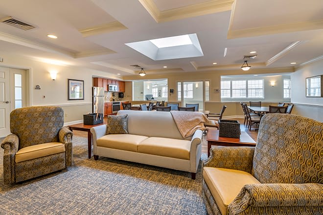 A spacious and well-lit living room featuring comfortable sofas and armchairs, with a skylight and large windows providing ample natural light.