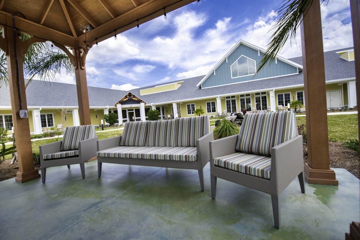 A cozy outdoor seating area with striped cushions under a gazebo, overlooking a building against a partly cloudy sky.