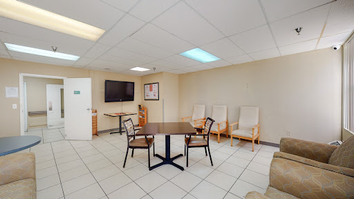 A spacious and well-lit waiting room featuring a table, chairs, and a television.