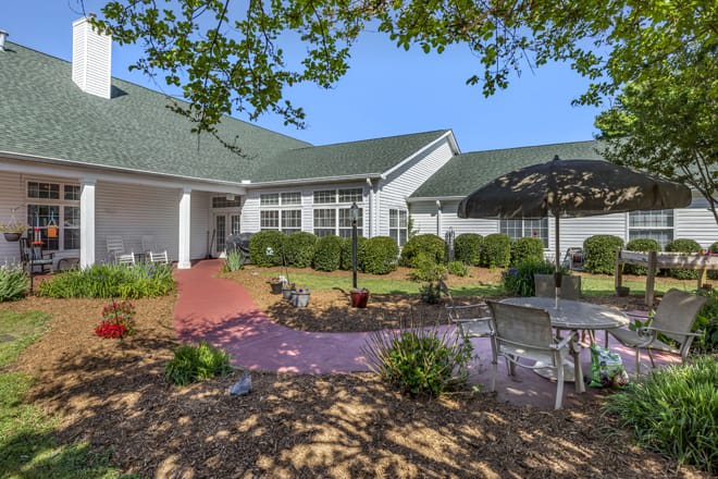 A sunny patio area outside a building, featuring outdoor seating and lush landscaping.