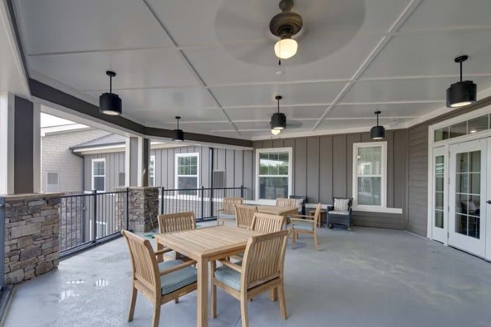 A covered patio area with wooden tables and chairs, featuring ceiling fans for comfort.