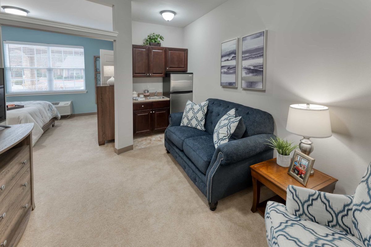 A cozy living room with a blue sofa, kitchenette, and decorative elements.