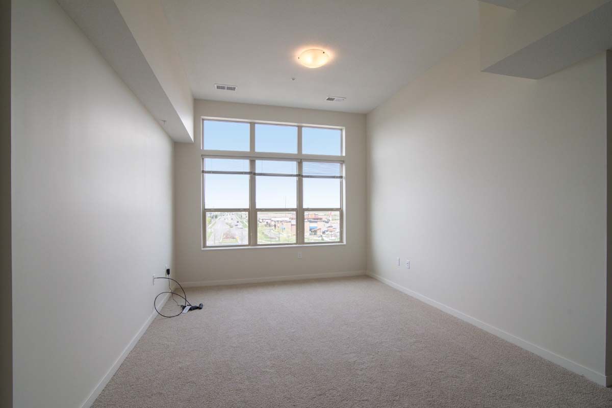 A minimalist empty room with a large window and carpeted floor.