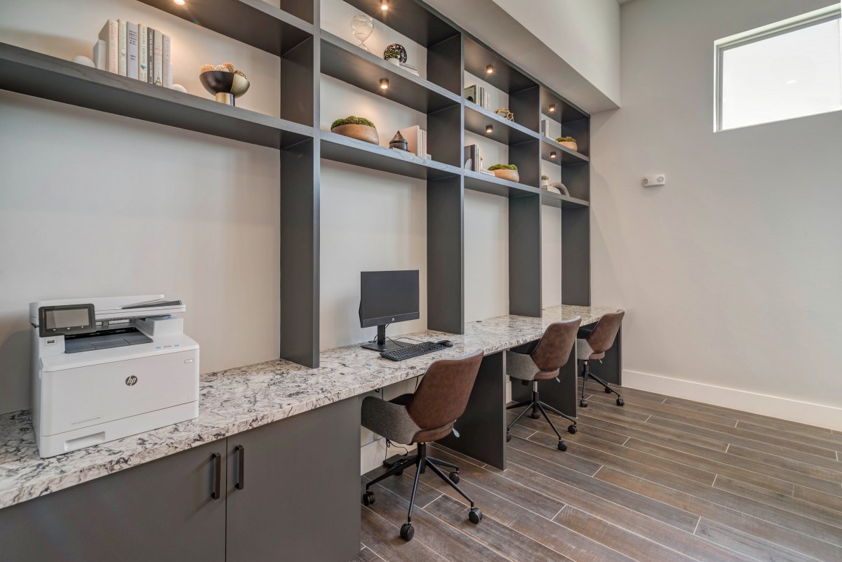 A modern office workspace featuring multiple desks with computers and chairs, complemented by tall shelving units.